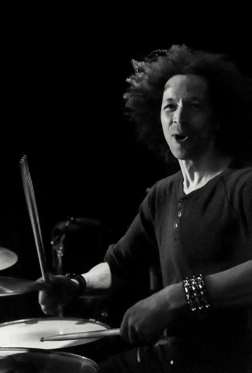 Black and white action shot of Zack smiling while he plays drums.